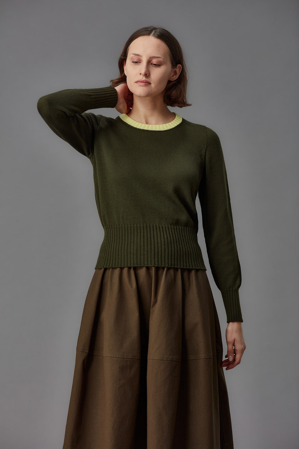 Woman wearing a green sweater with a yellow collar and brown skirt against a gray background