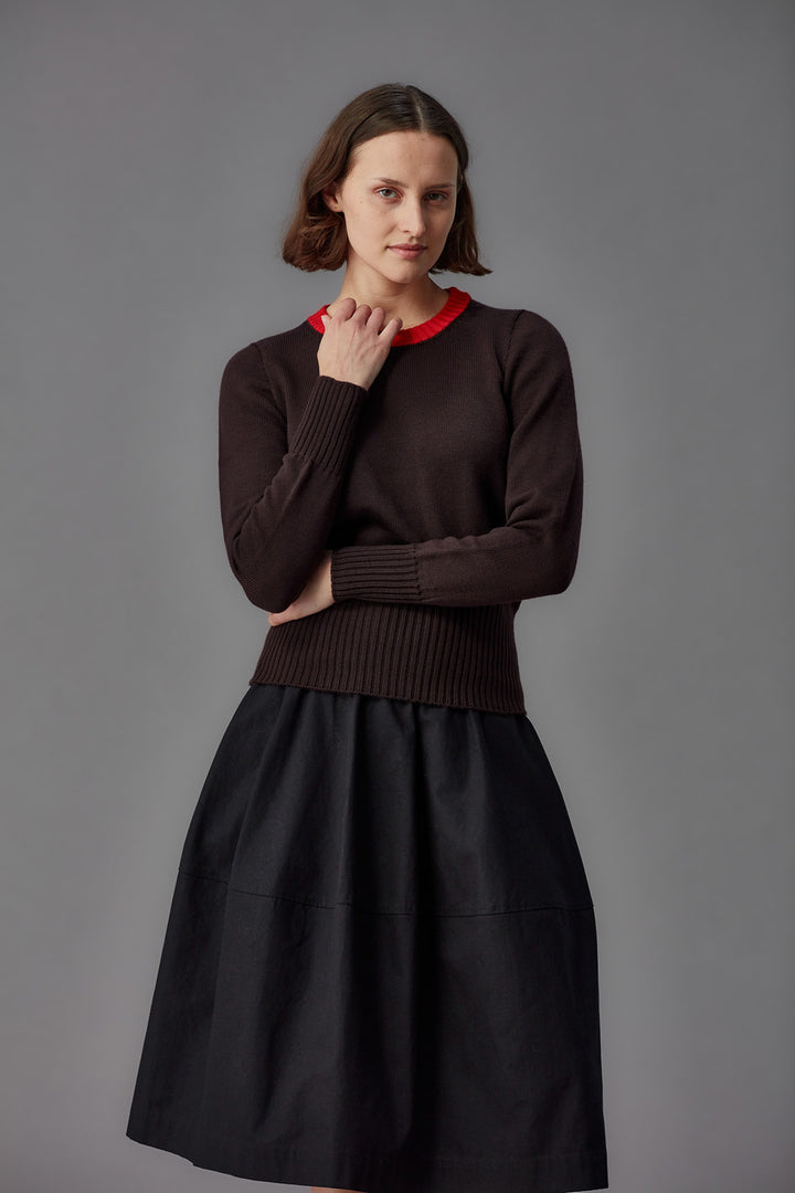 Woman wearing a brown sweater with a red collar and black skirt against a gray background