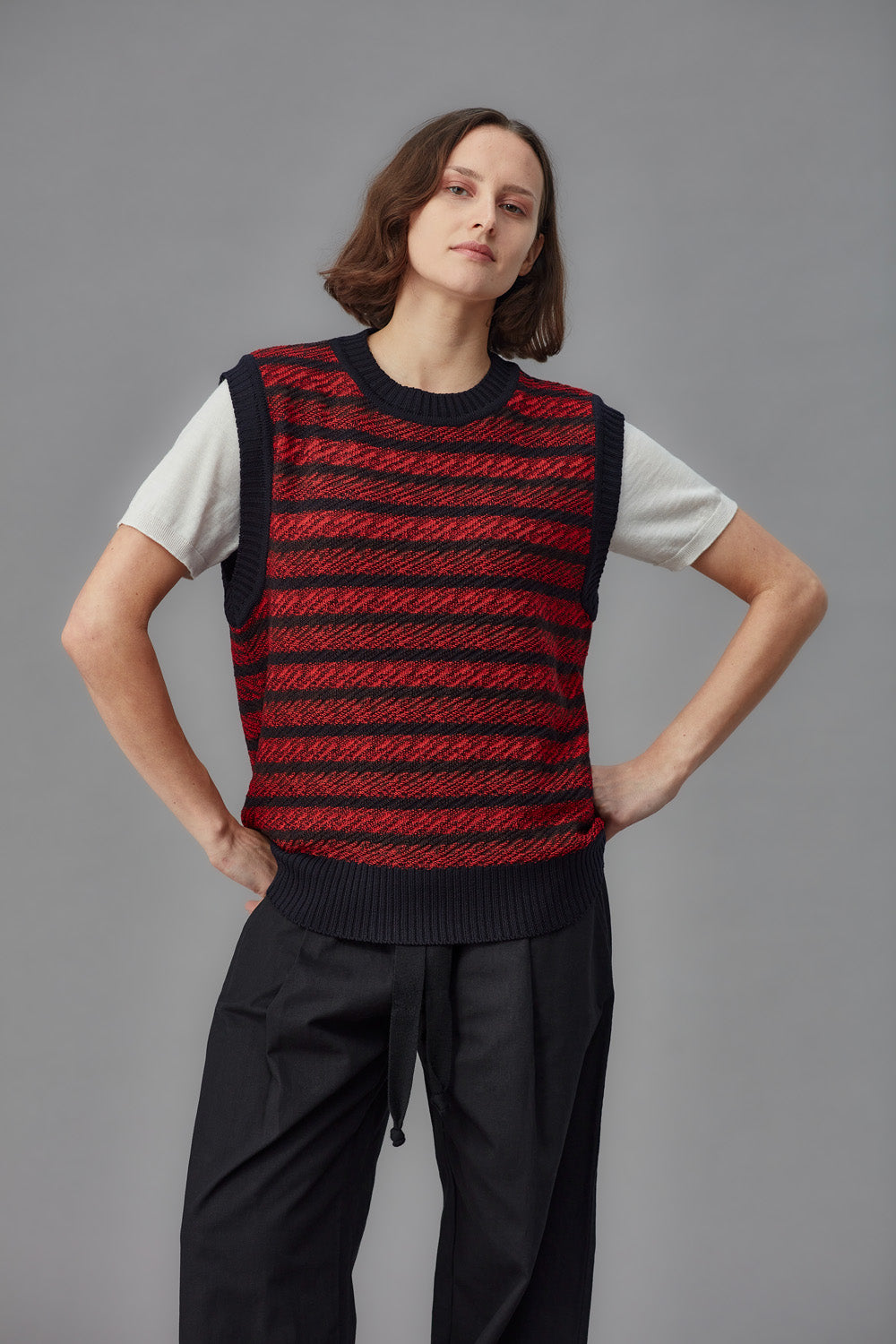 Woman wearing a red and black striped vest over a white shirt on a gray background