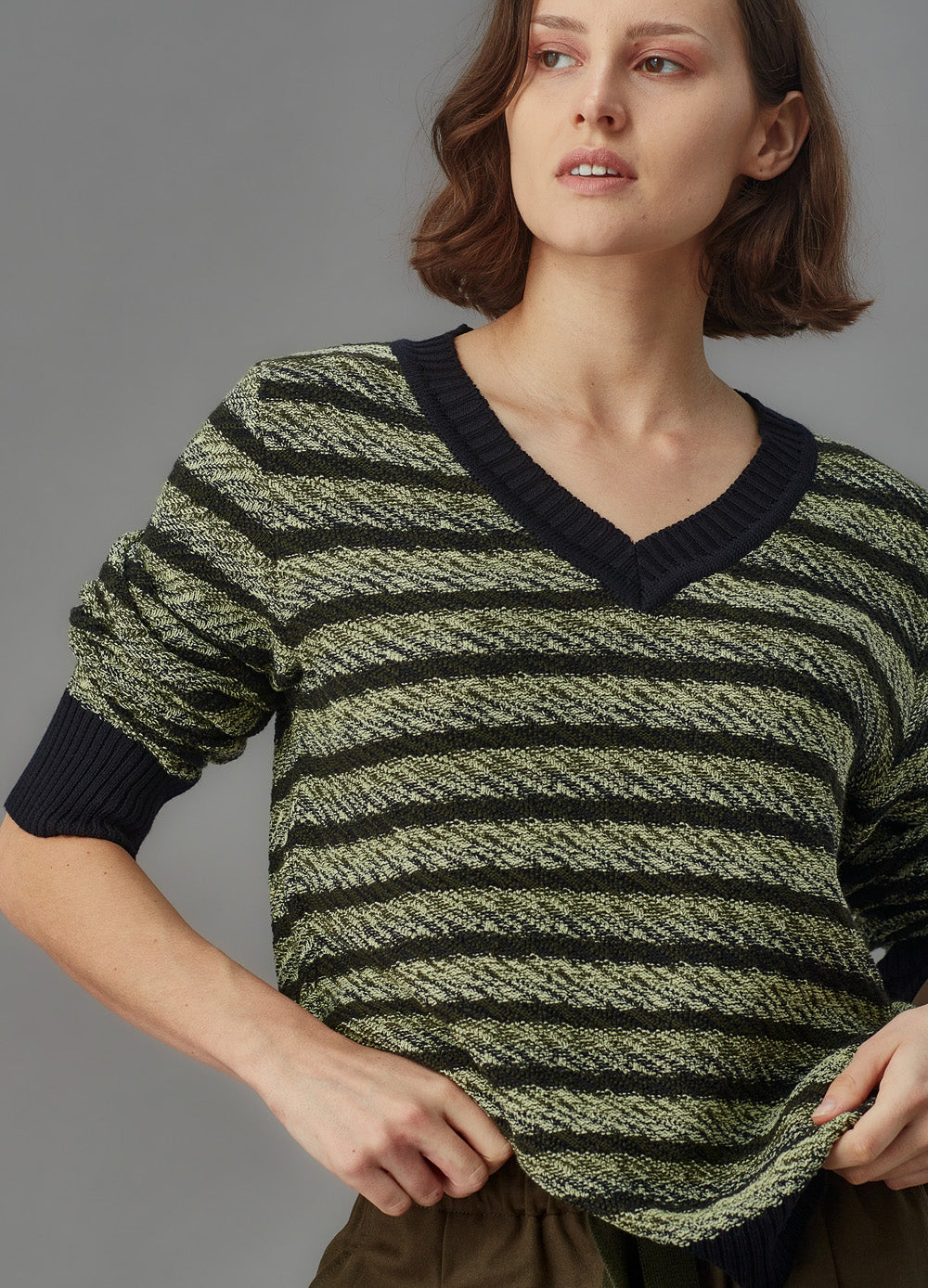 Woman wearing a green and black striped sweater against a gray background