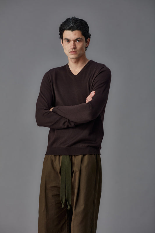 Man wearing a brown long-sleeve shirt and wide-leg pants against a gray background