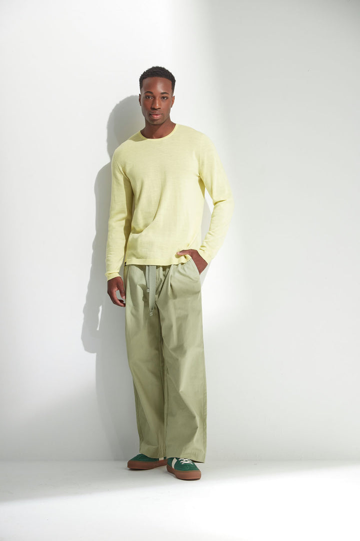 Man wearing a yellow sweater and green pants against a white background