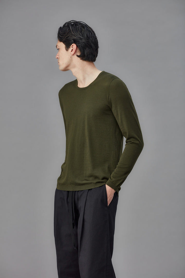 Man wearing an olive green long-sleeve shirt and black pants against a gray background