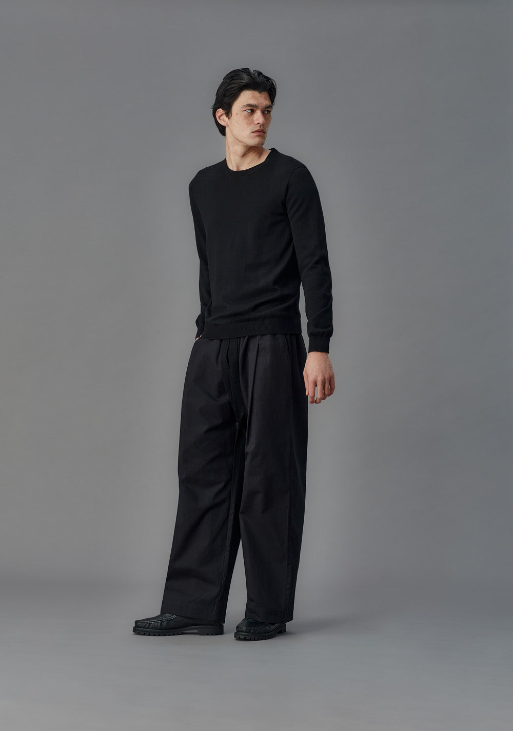 Man wearing a black outfit against a gray background