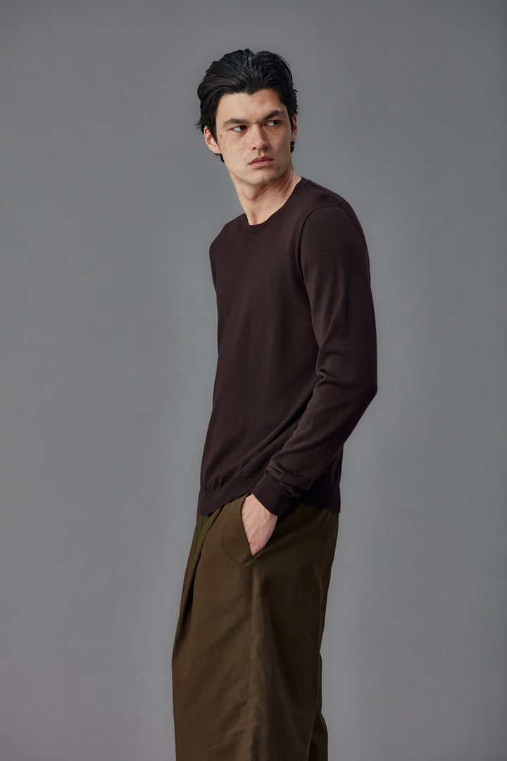 Man wearing a brown long-sleeve shirt and brown pants against a gray background