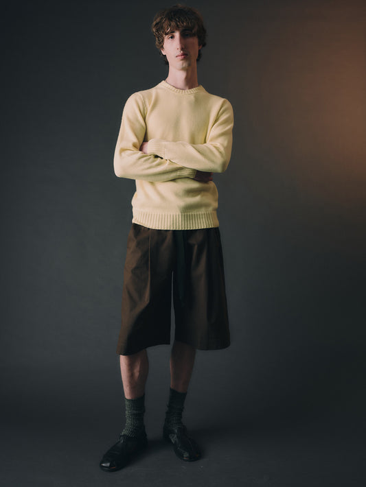 Man wearing a light yellow cashmere sweater and dark shorts against a gradient background