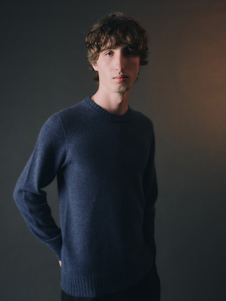 Man wearing a blue cashmere sweater against a dark background