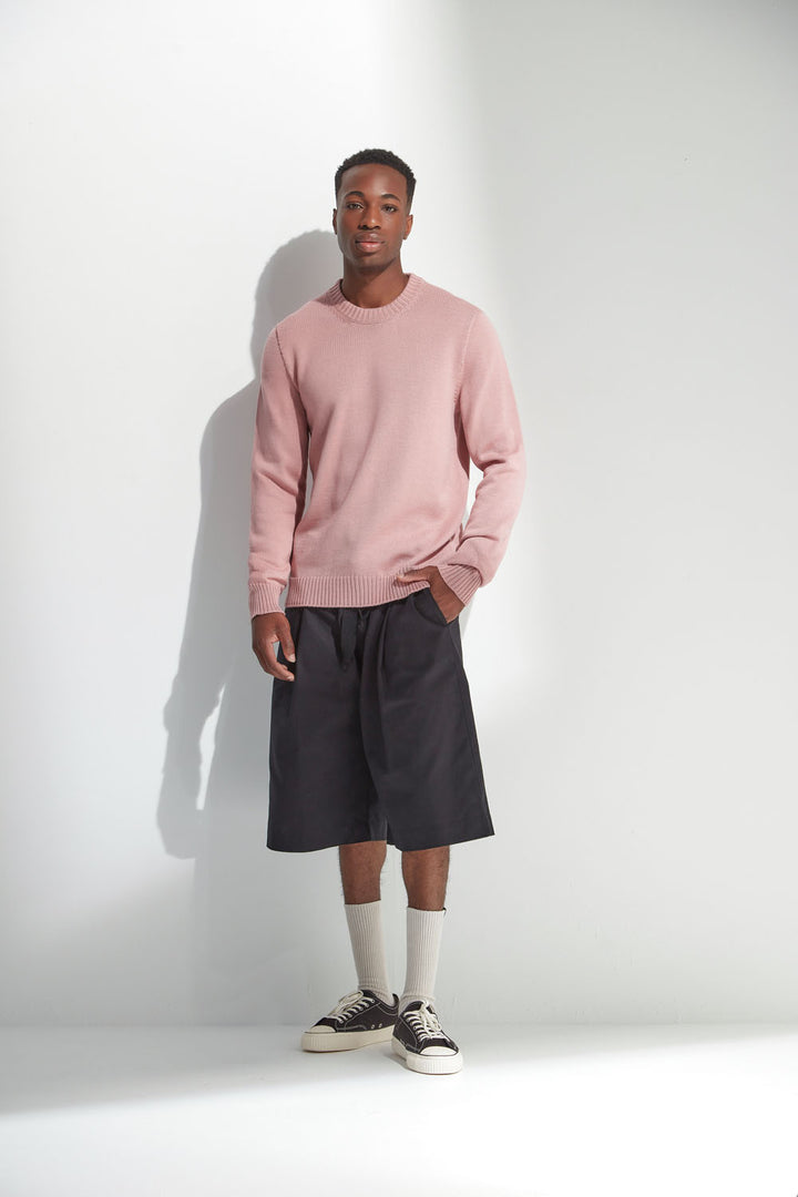 Man wearing a pink sweater, black shorts, and sneakers against a white background