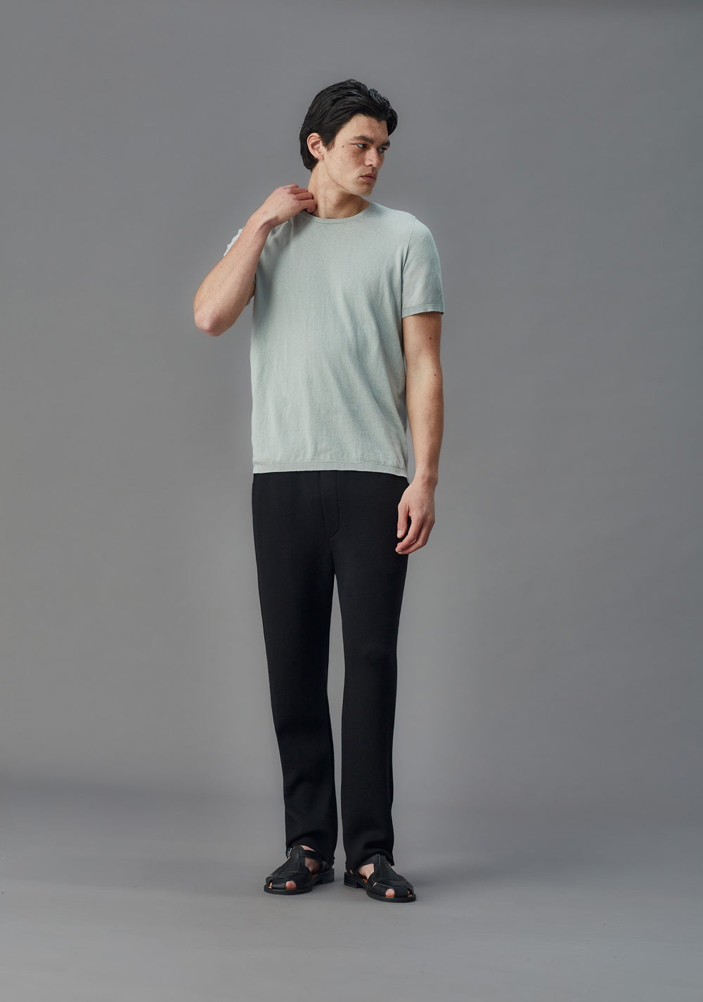 Man wearing a light blue t-shirt and black knit pants on a gray background