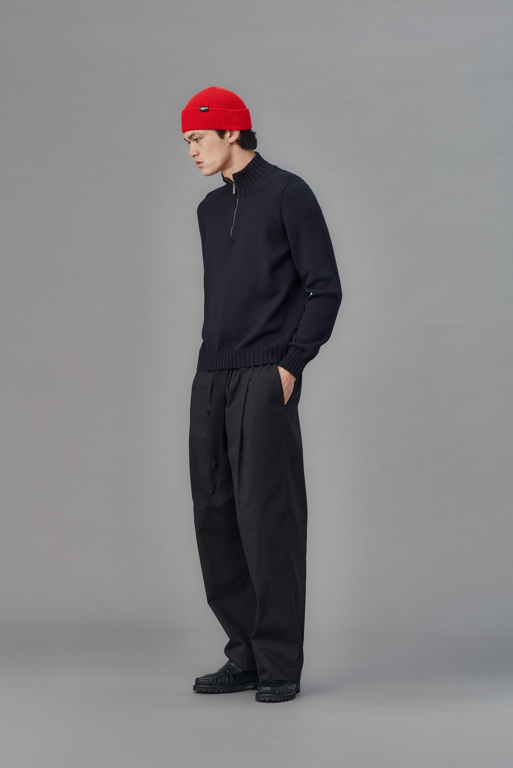 Person wearing a black outfit with a red beanie on a gray background