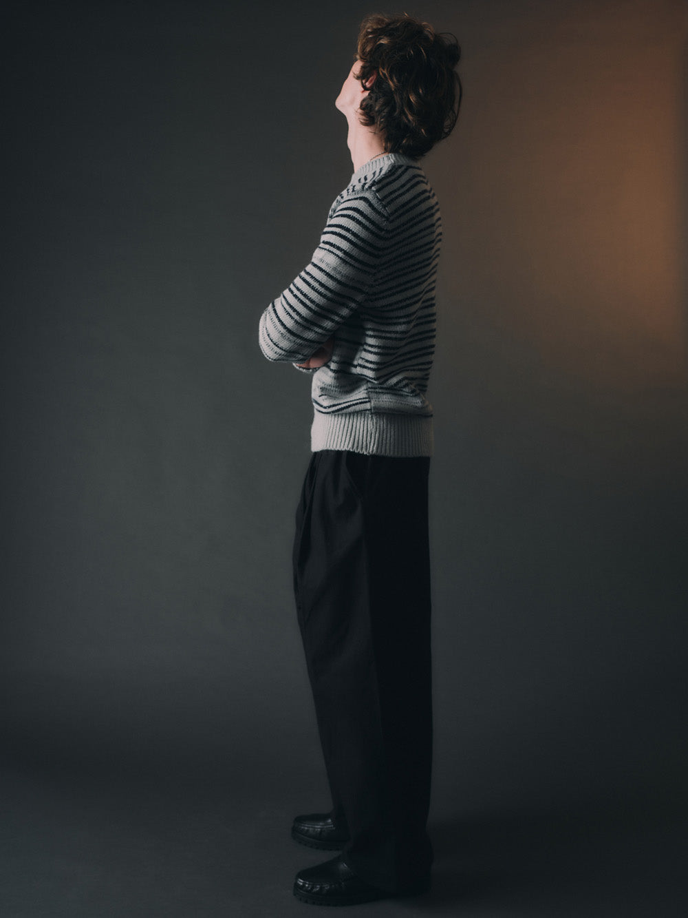 Person wearing a striped sweater and dark pants against a plain background