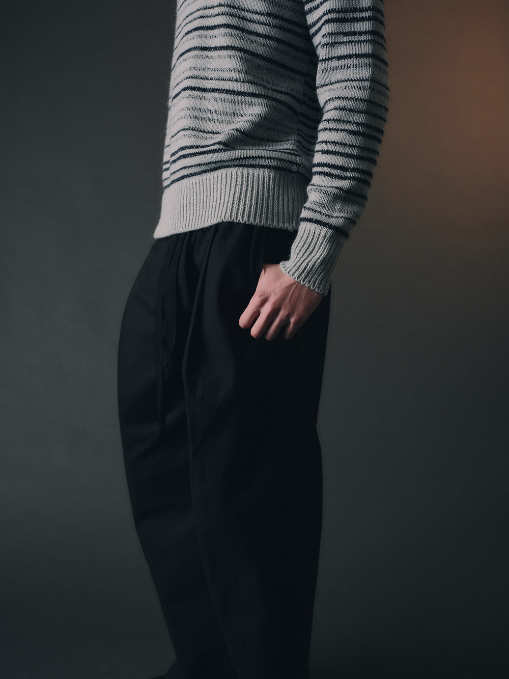 Person wearing a gray striped sweater and black pants against a dark background
