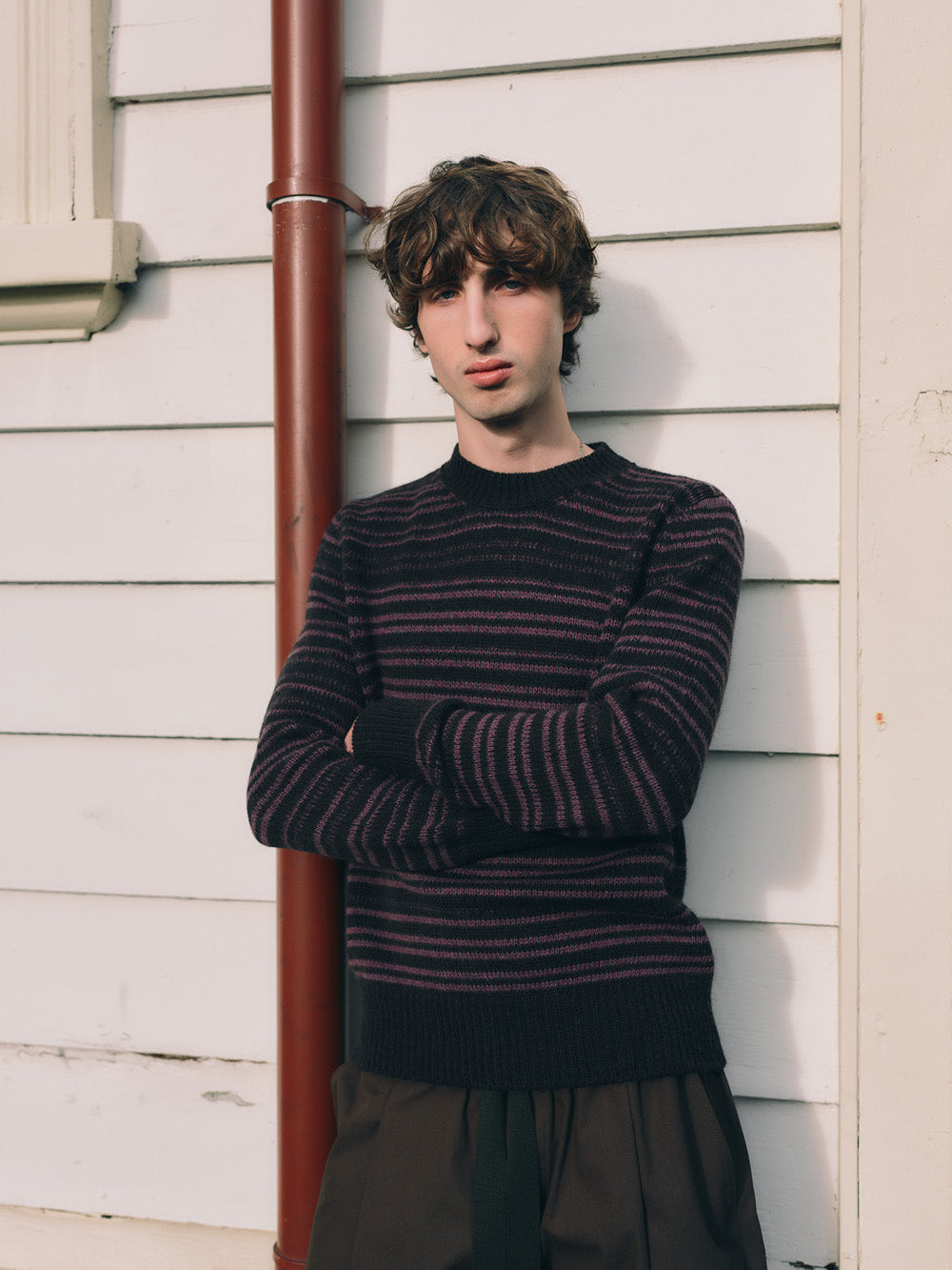 Person wearing a striped sweater leaning against a house exterior.