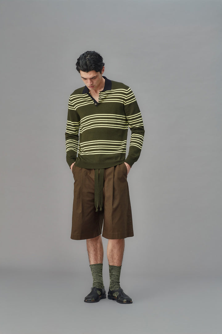Man wearing a green striped sweater and brown shorts on a gray background