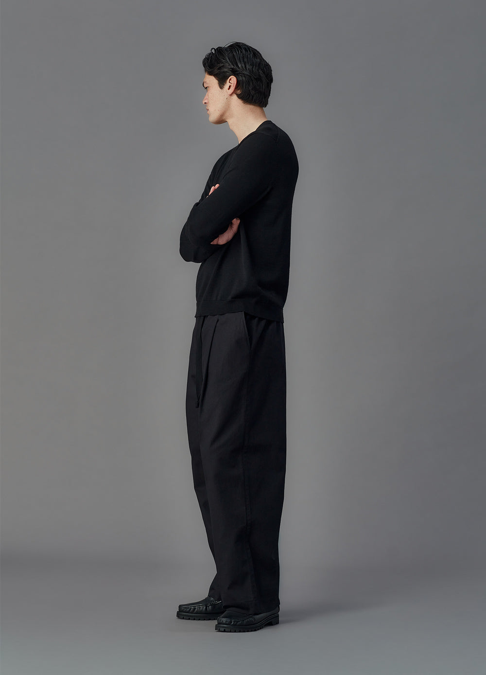 Person wearing a black outfit standing against a gray background