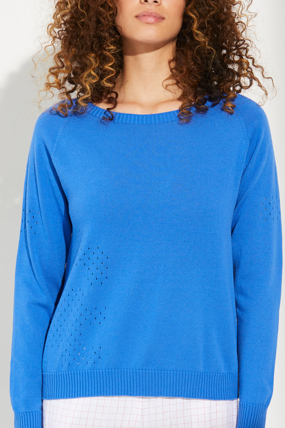 A woman standing wearing a sky diver-coloured Standard Issue Cotton Eyelet A Line sweater.